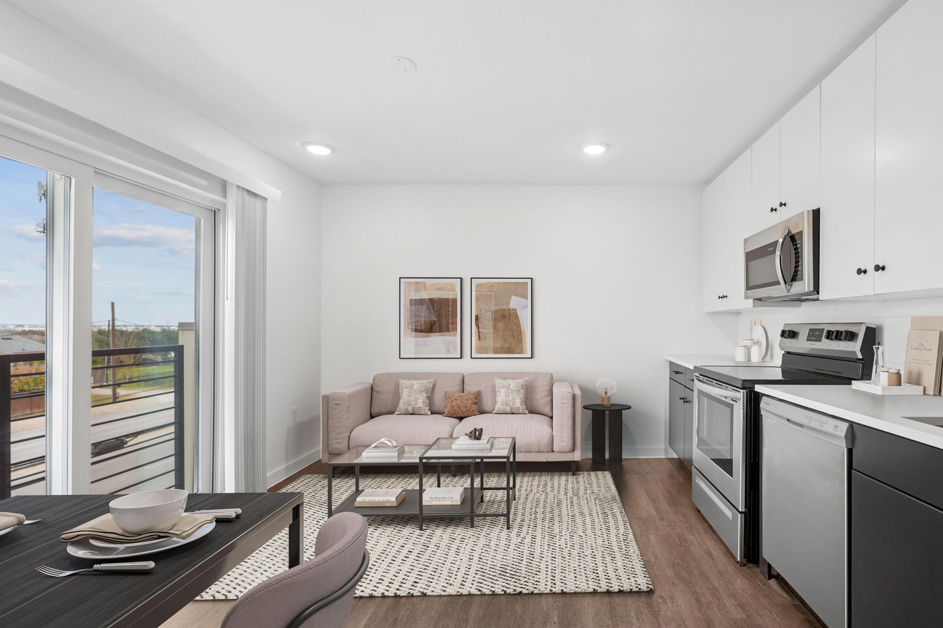 A modern open-concept apartment with a living area featuring a beige sofa, patterned rug, and an adjacent kitchen.