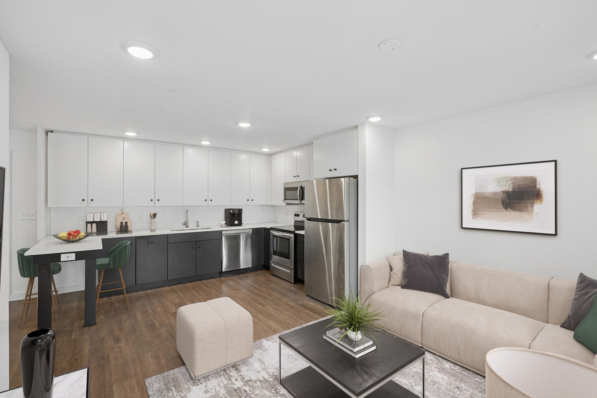 Modern studio apartment with a sleek kitchen featuring white upper cabinets, dark lower cabinets, and an adjacent sofa.