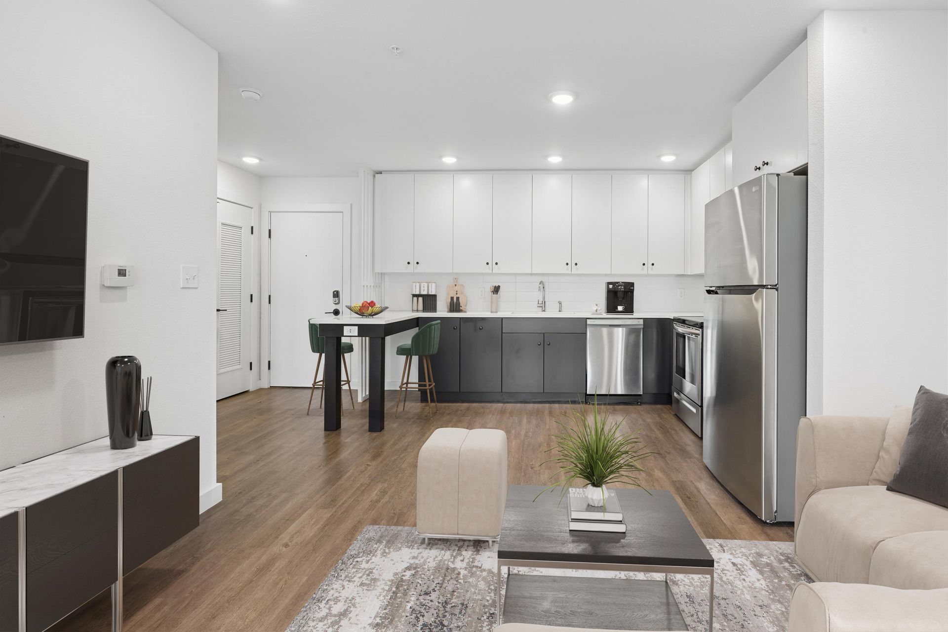 A modern, open-concept living area featuring a kitchen with white upper cabinets, dark base cabinets, and a dining island.