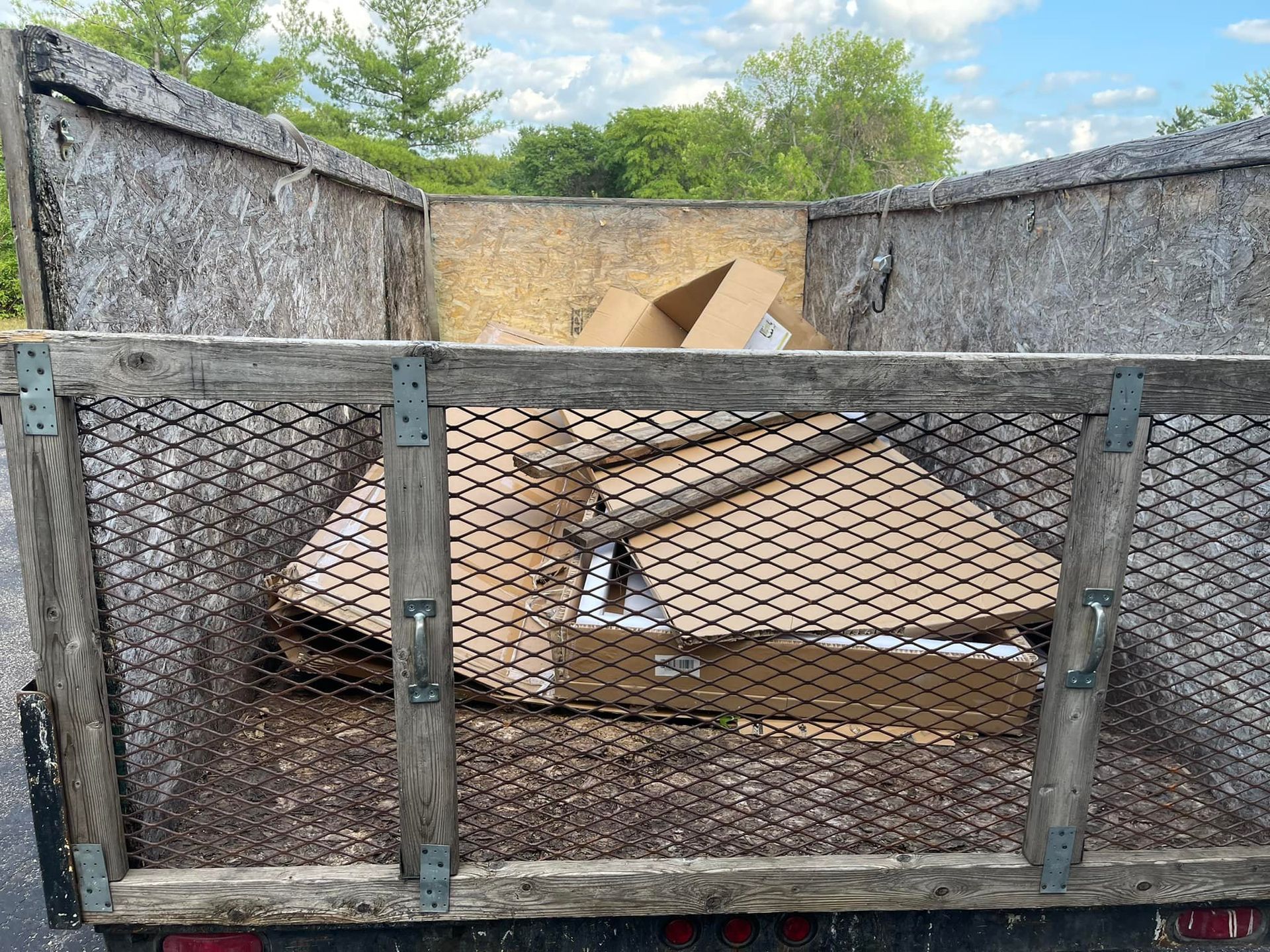 Cardboard boxes inside a wooden trailer with wire mesh sides, against a blue sky.