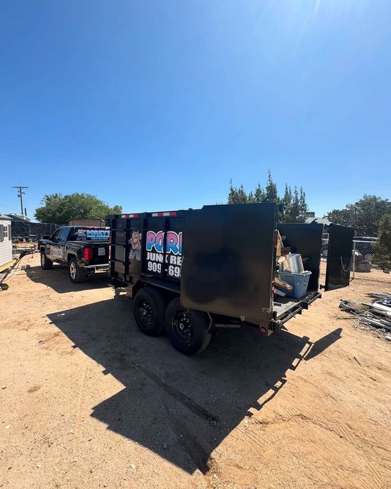 Black pickup truck pulling a loaded black trailer in a dirt lot under a clear sky.