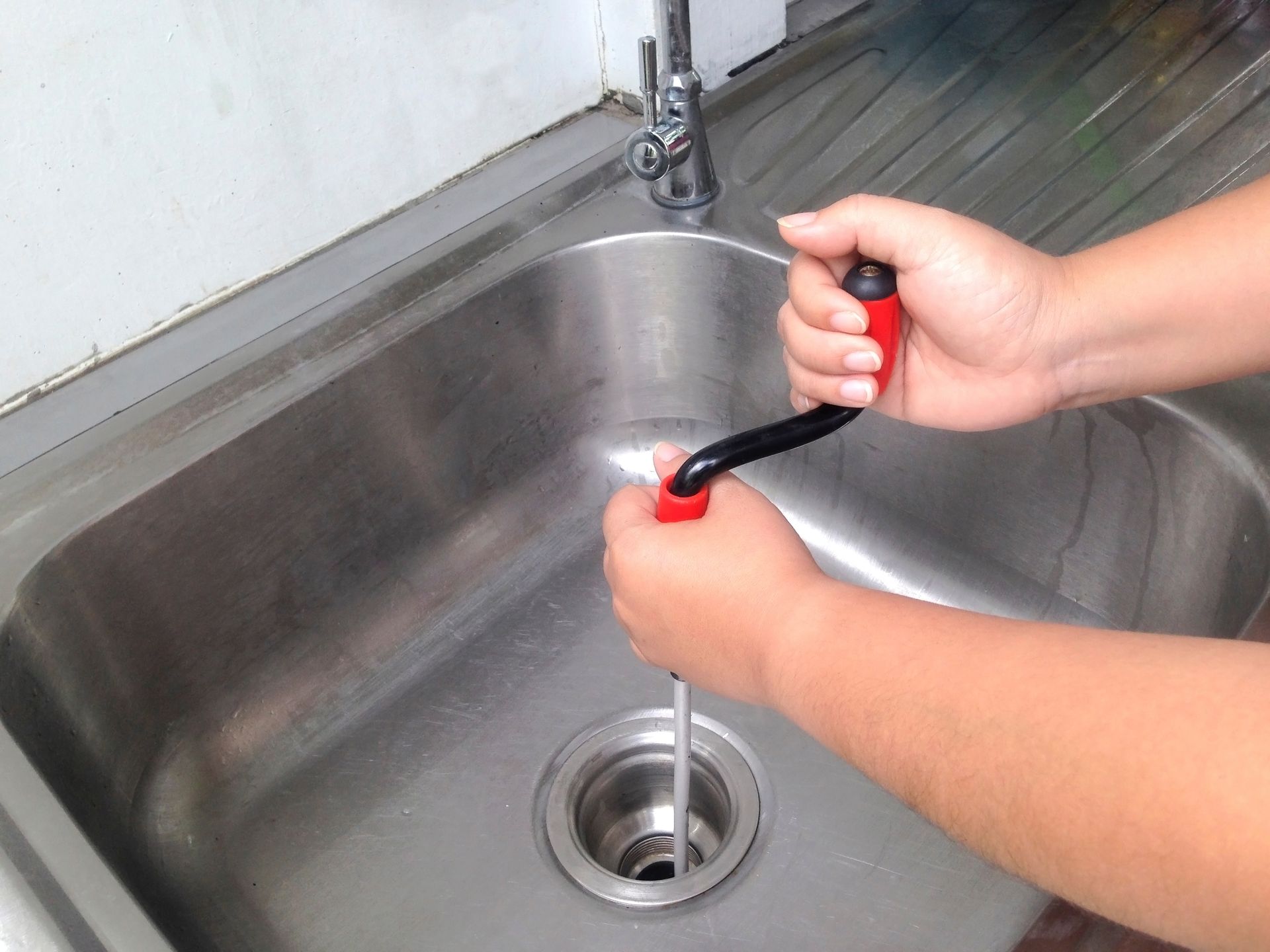 A person is using a snake to drain a sink.