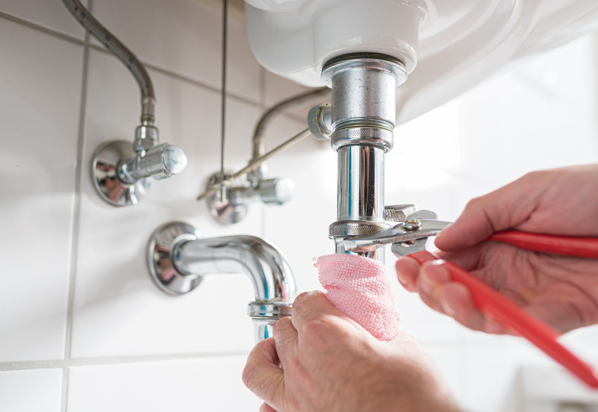 A person is fixing a sink pipe with a wrench.