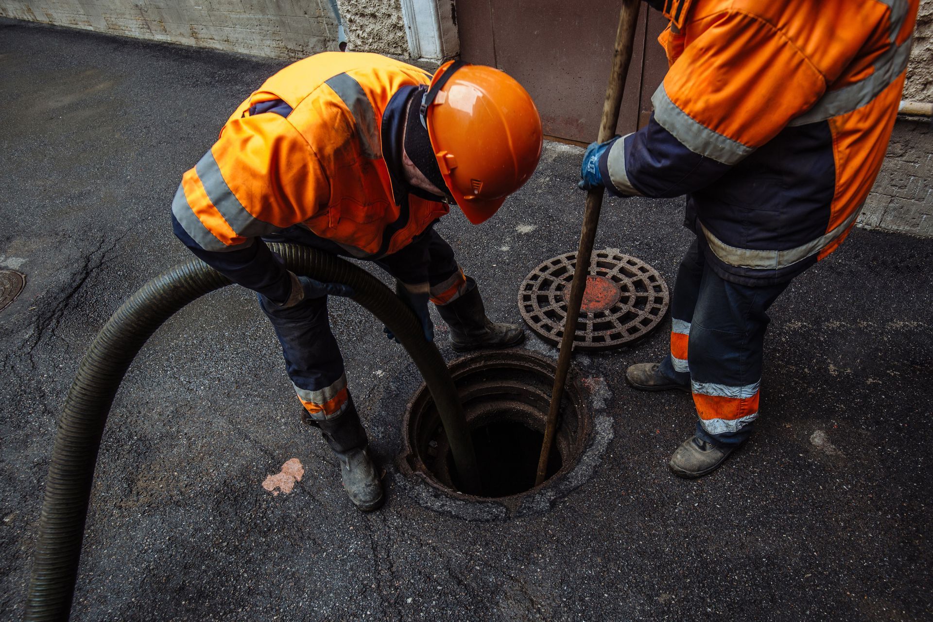 Two men are cleaning a manhole cover with a hose.