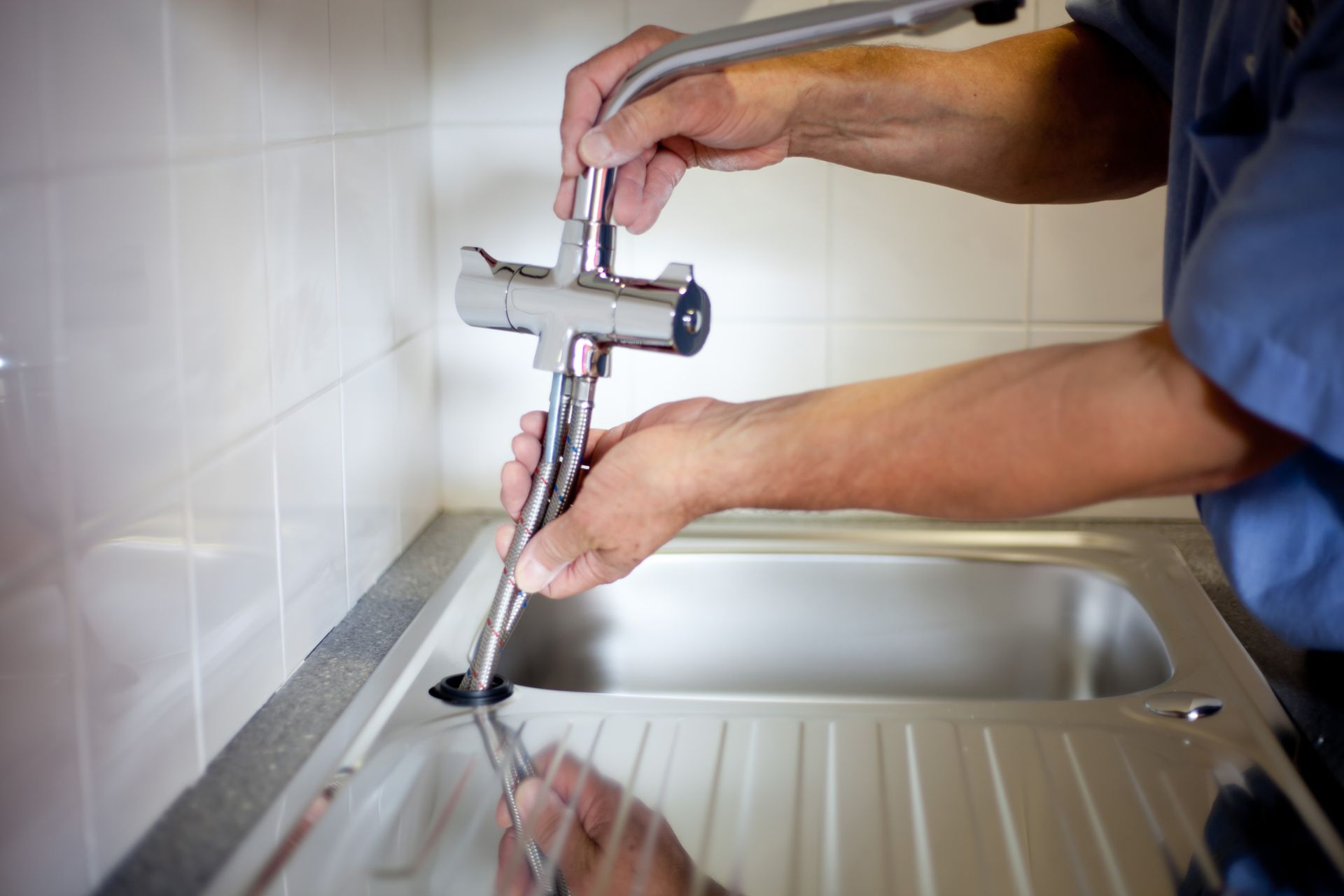 A man is fixing a faucet in a kitchen with a wrench.
