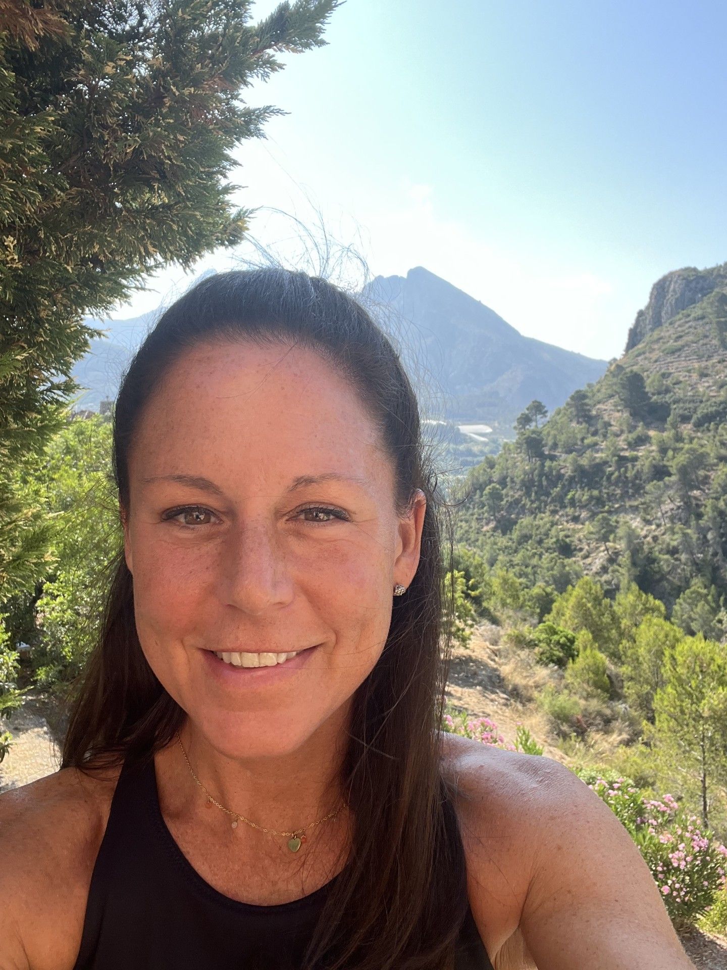 Woman with gray hair and hoop earrings, smiling, in front of a light background.