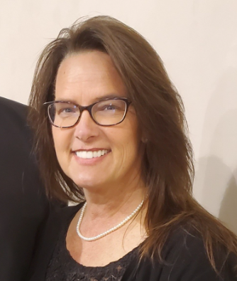 Person wearing glasses and a beanie holding a Boston Terrier in a yellow sweater, orange background.