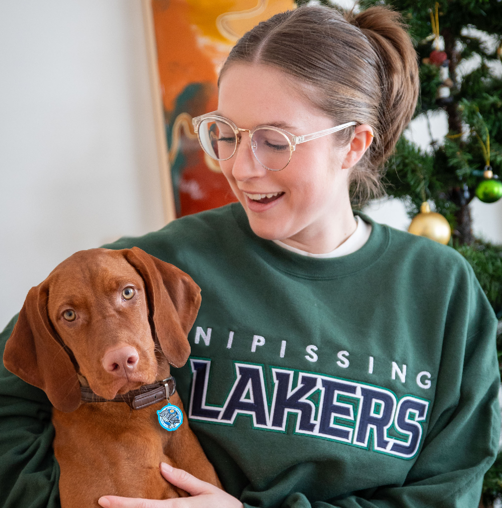 Woman in green sweatshirt with dog, near Christmas tree.