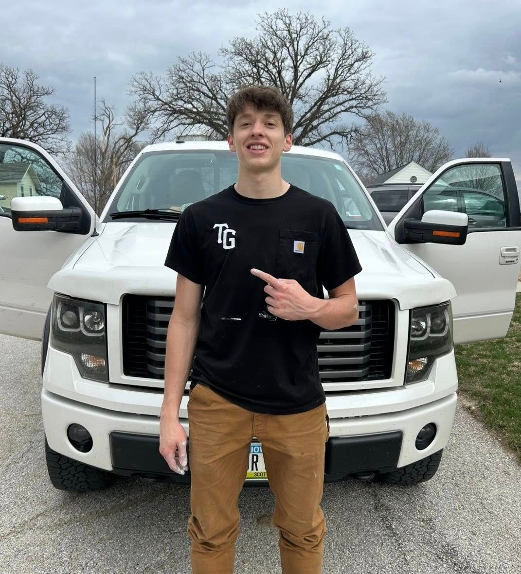 A young man is standing in front of a white truck.