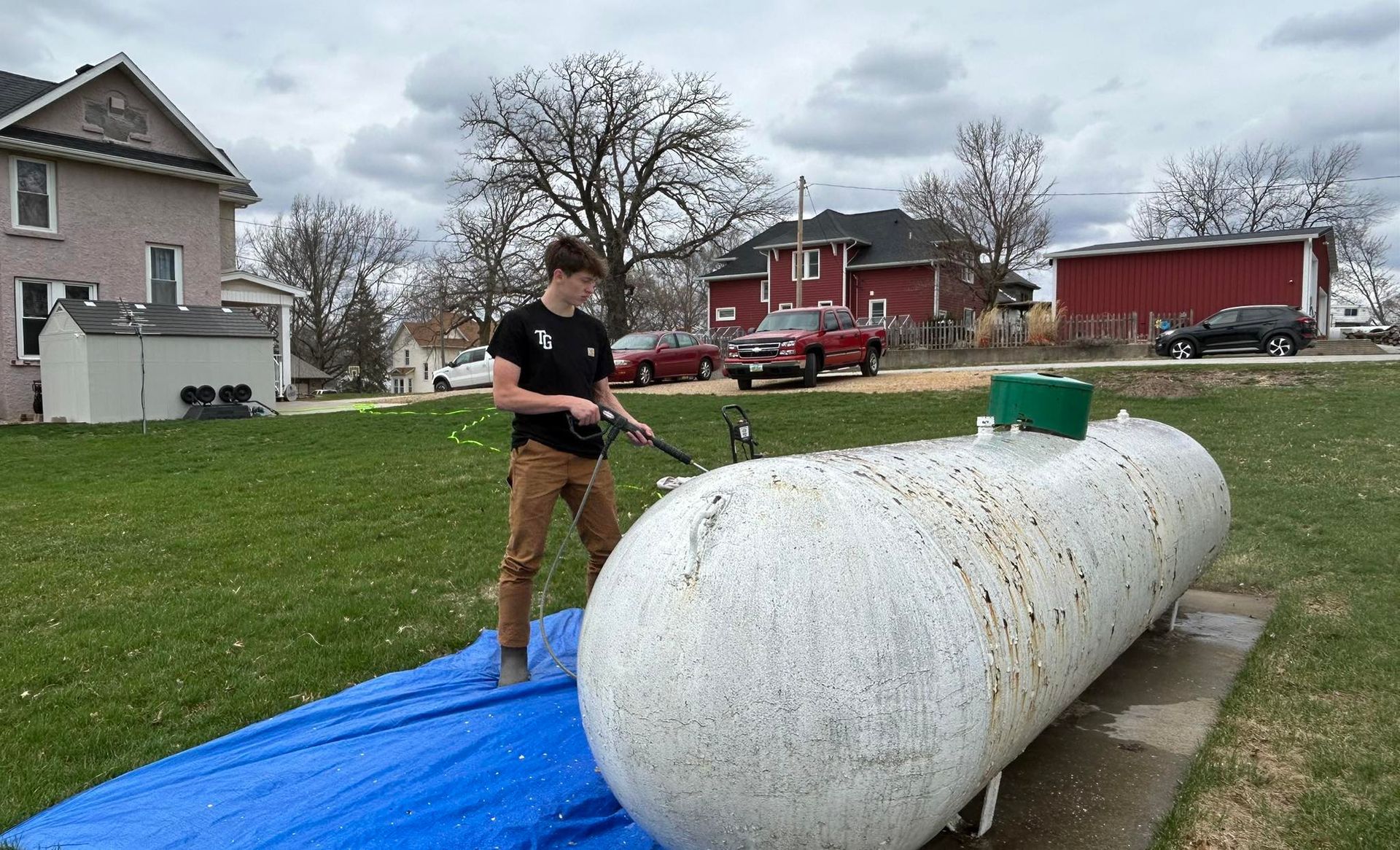 A man is standing next to a large white propane tank.