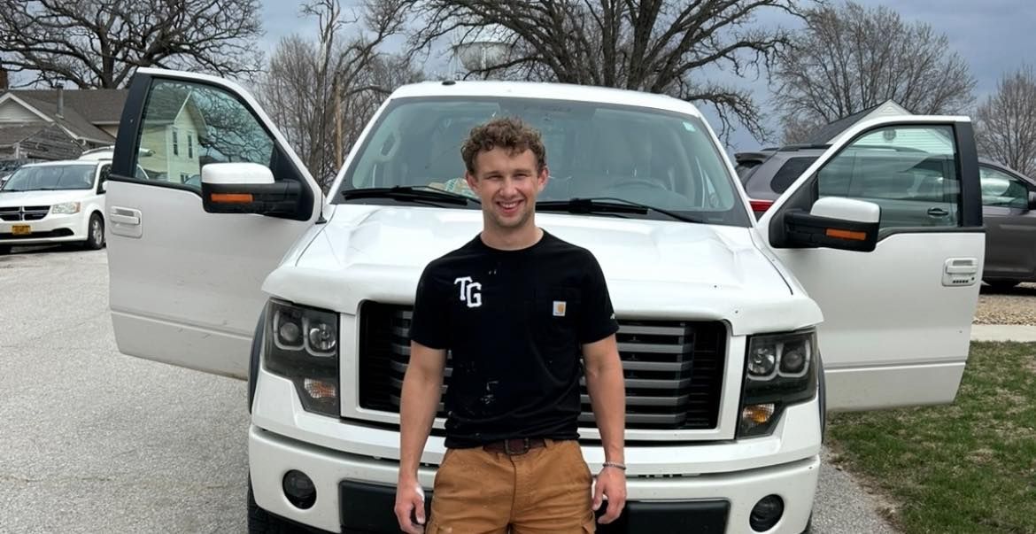 A man is standing in front of a white truck with its doors open.