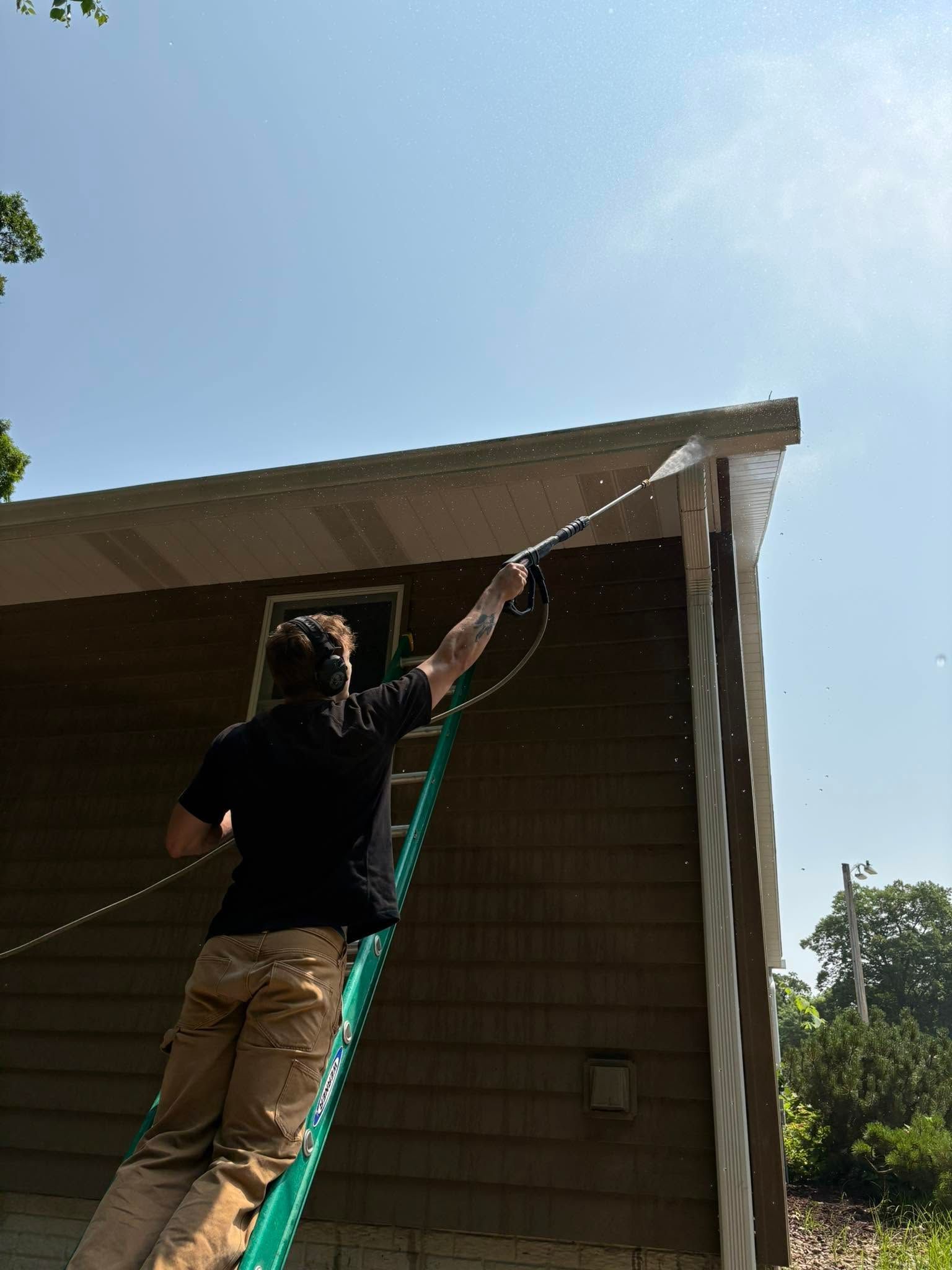 A man is standing on a ladder spraying a house with a hose.