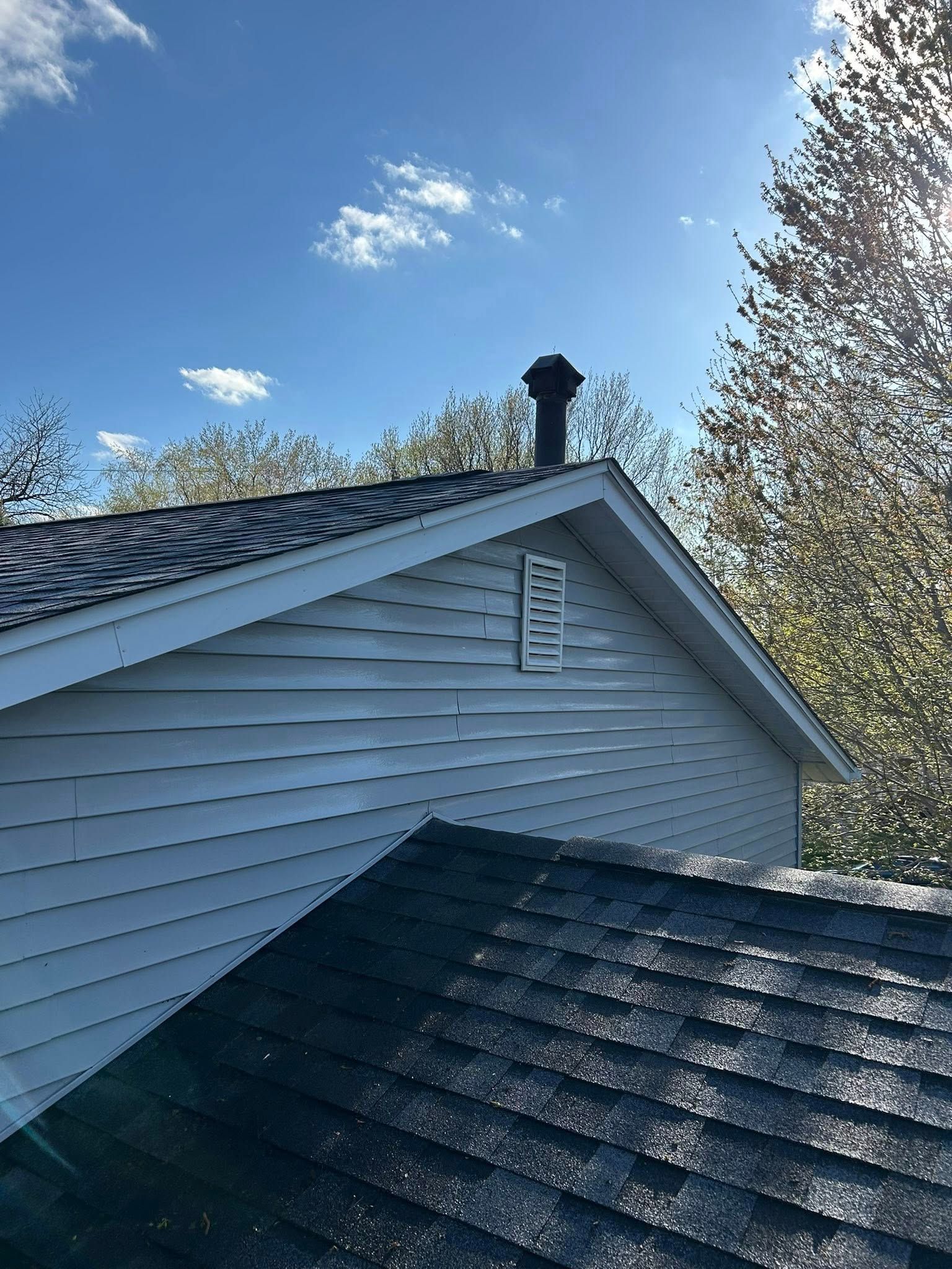 A white house with a black roof and a chimney on top of it.