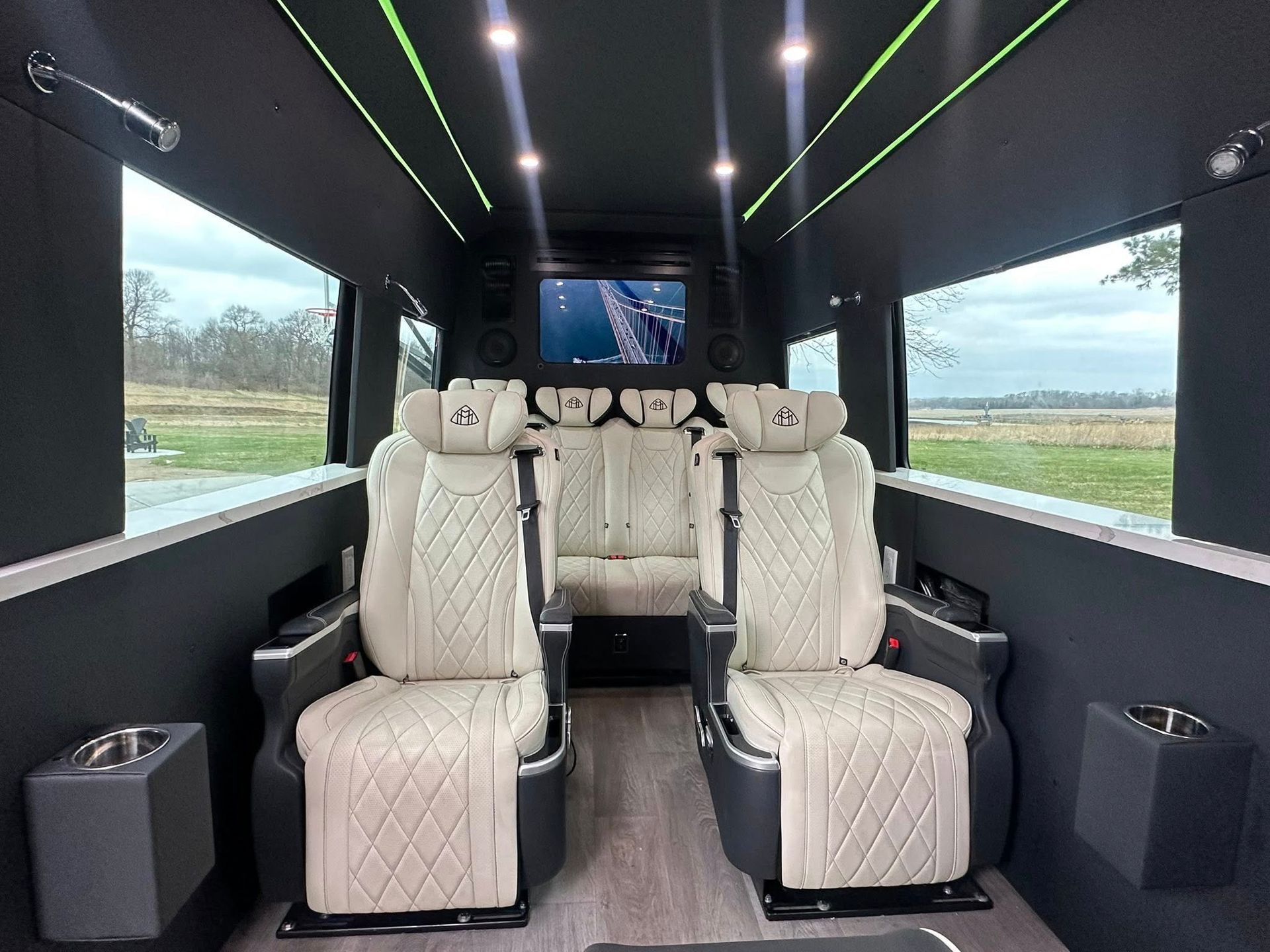 The interior of a van with white seats and a flat screen tv.