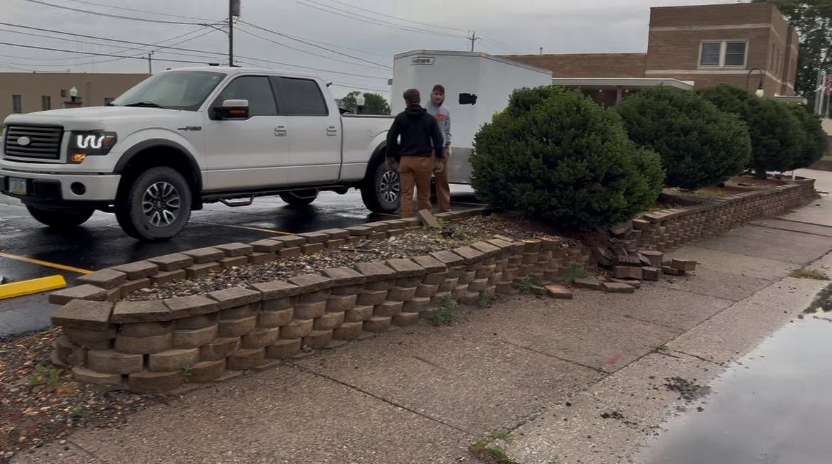 A white truck is parked on the side of the road next to a brick wall.