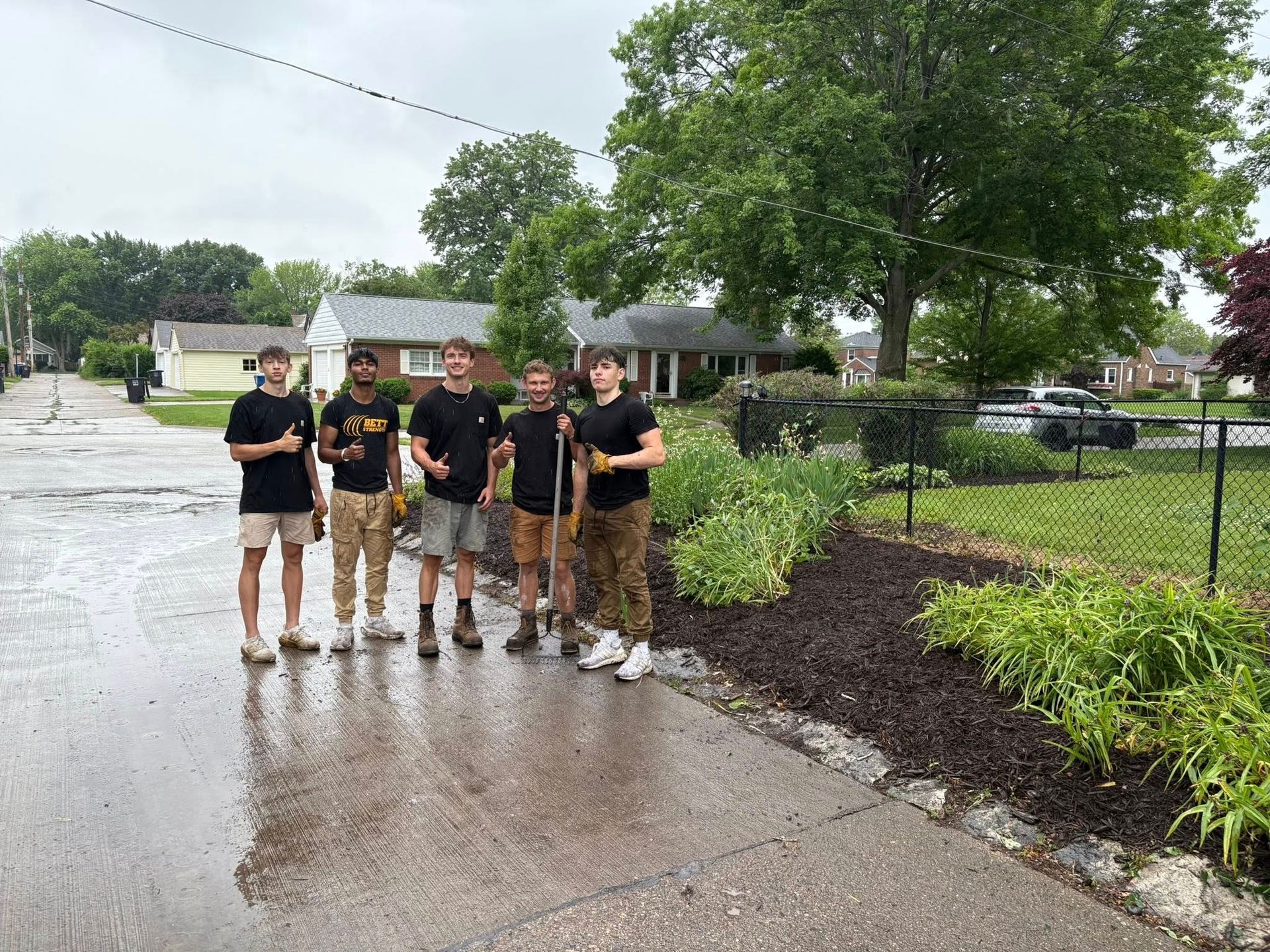 A group of young men are standing on the side of a road in the rain.