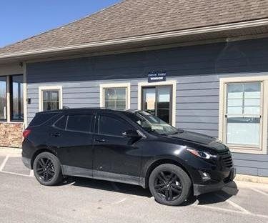 Black SUV parked in front of a blue building with windows. Black tires and tinted windows are visible.