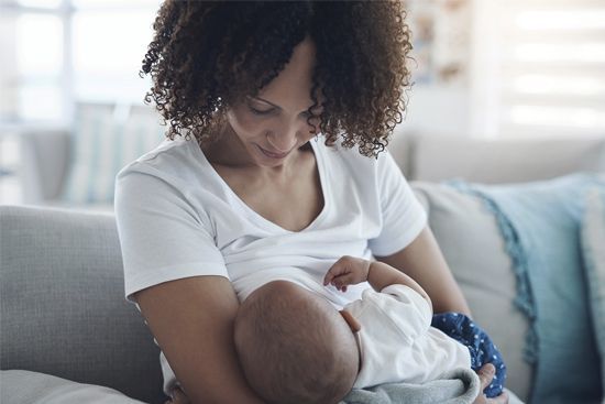 Woman in white shirt breastfeeding a baby on a couch.
