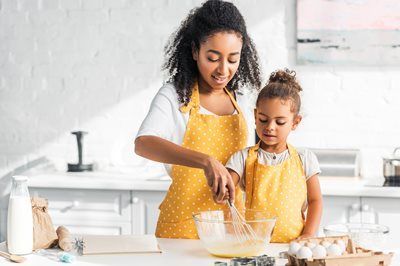 Woman and child whisking batter in kitchen, both wearing yellow aprons.