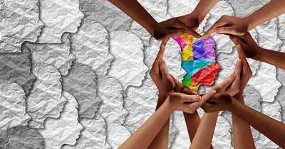 Hands of various skin tones holding a multicolored human head outline amidst grayscale profile silhouettes.
