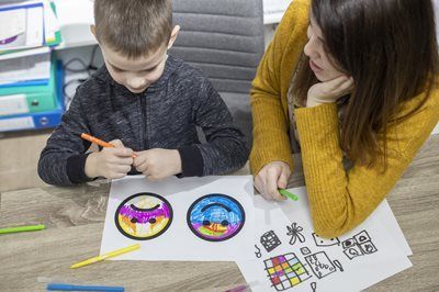 A child and person draw colorful emojis and other images with markers at a table.