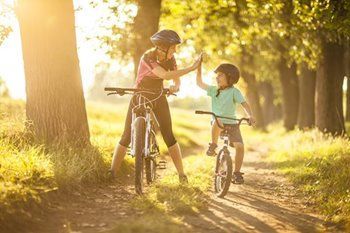 Woman and child on bikes high-fiving on a sunny path, wearing helmets.