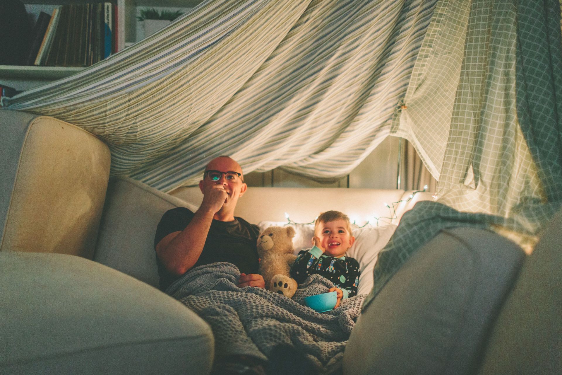 A man and a child are sitting on a couch under a canopy.