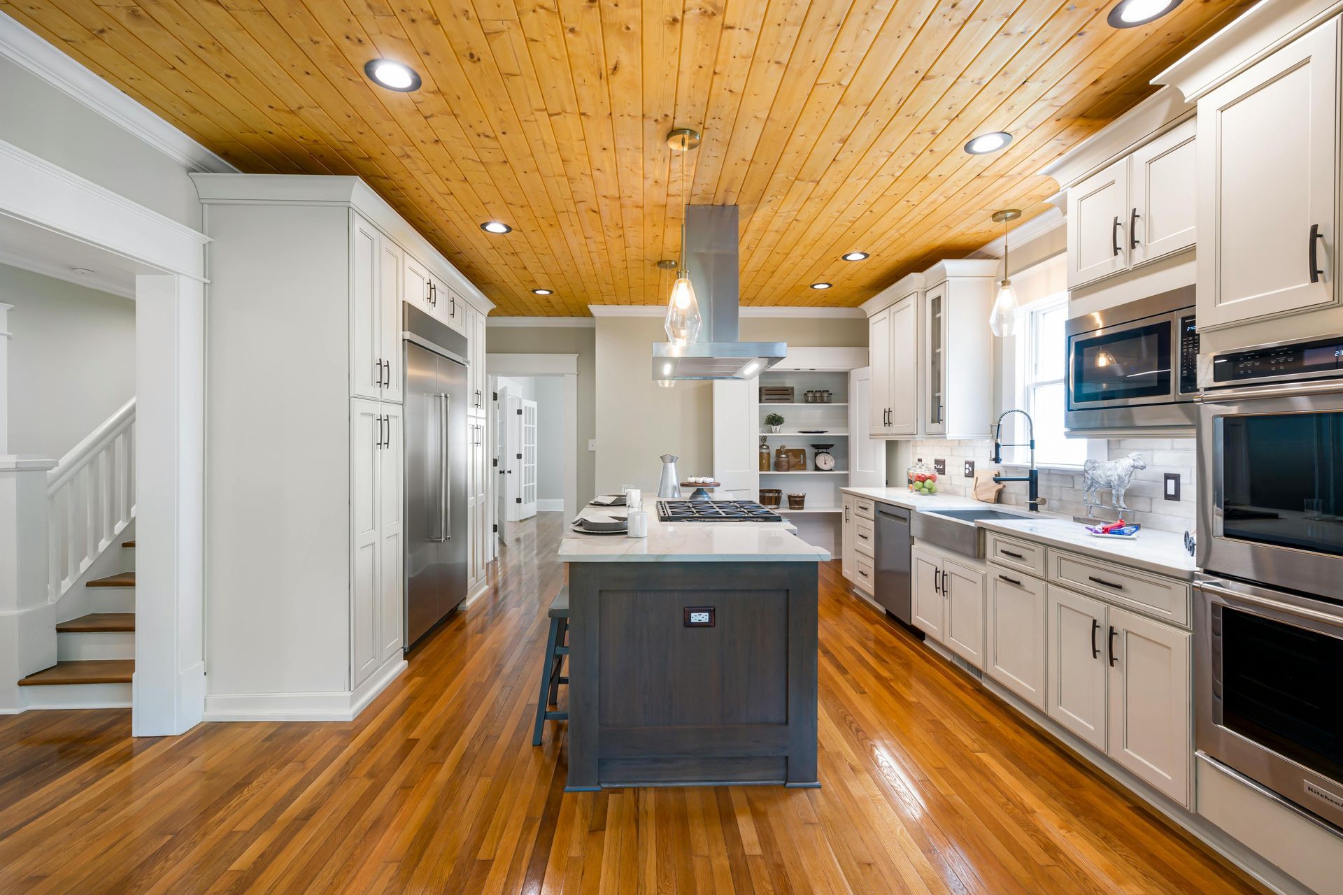 A modern kitchen featuring white cabinets, a dark gray island, stainless steel appliances, and a natural wood ceiling.