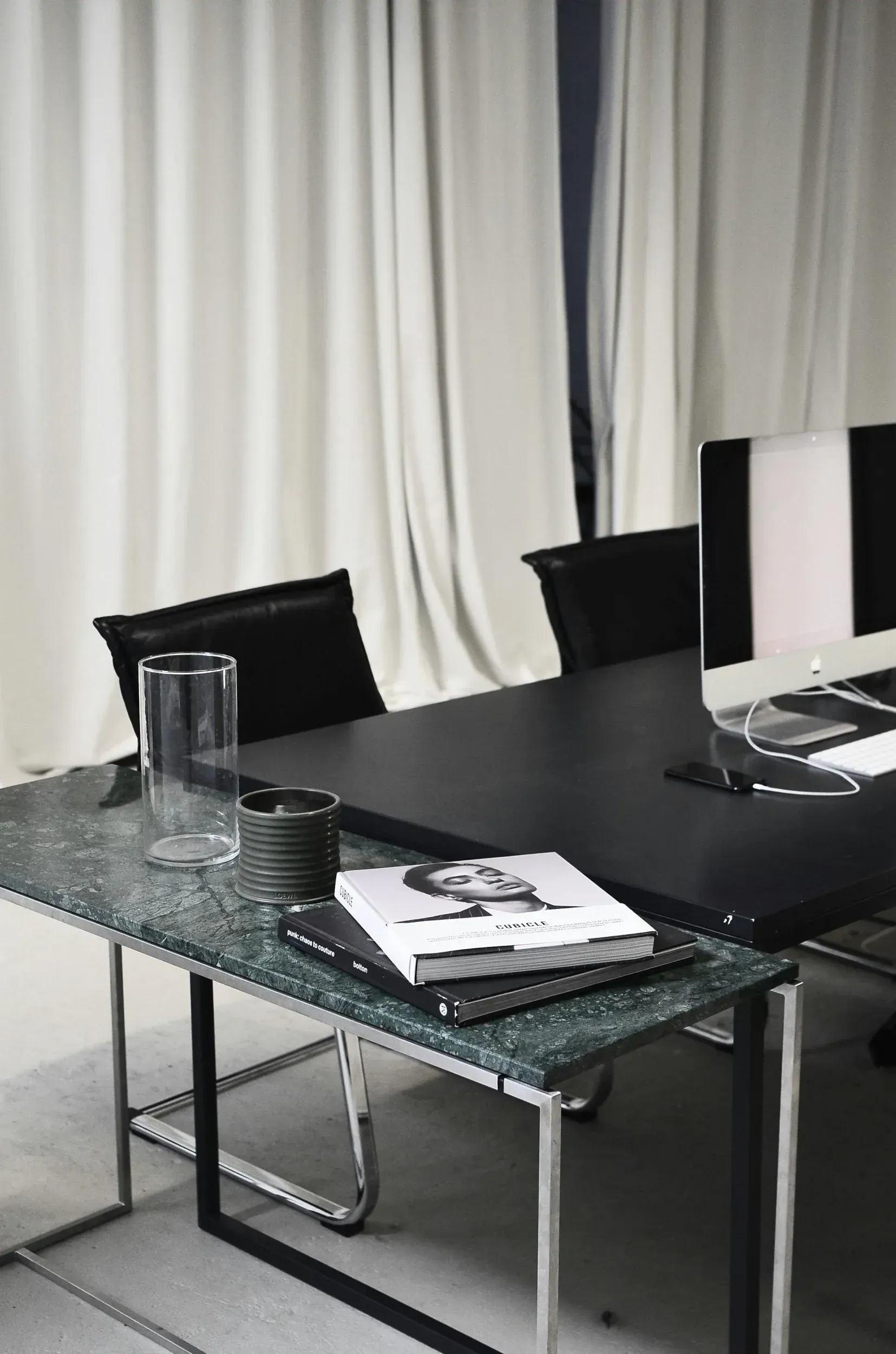 Desk in a modern office, green marble top, black desk, black chairs, white curtains in the background.