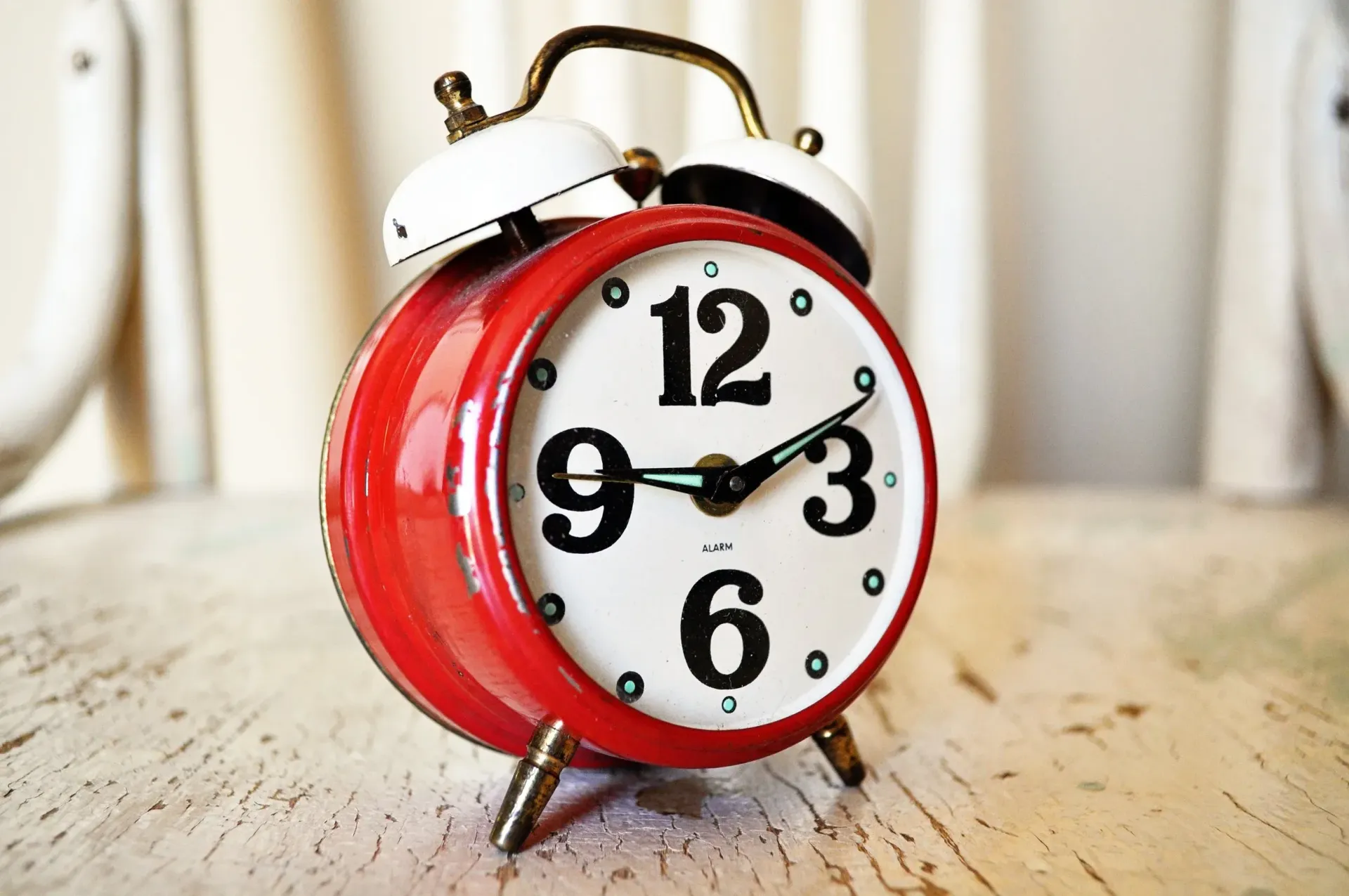 Red and white retro alarm clock on a distressed white wooden surface.