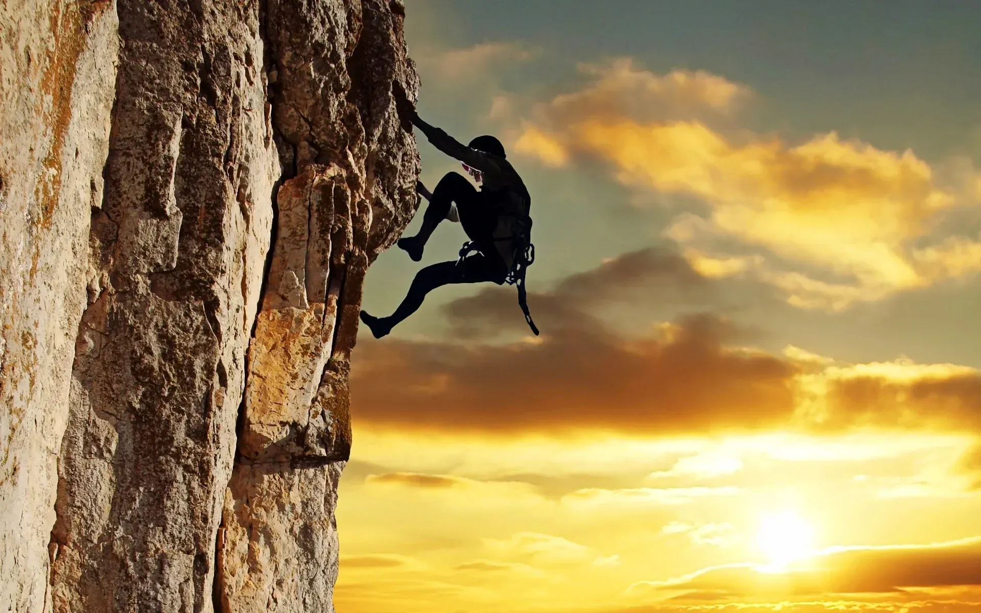 Rock climber ascends cliff at sunset.