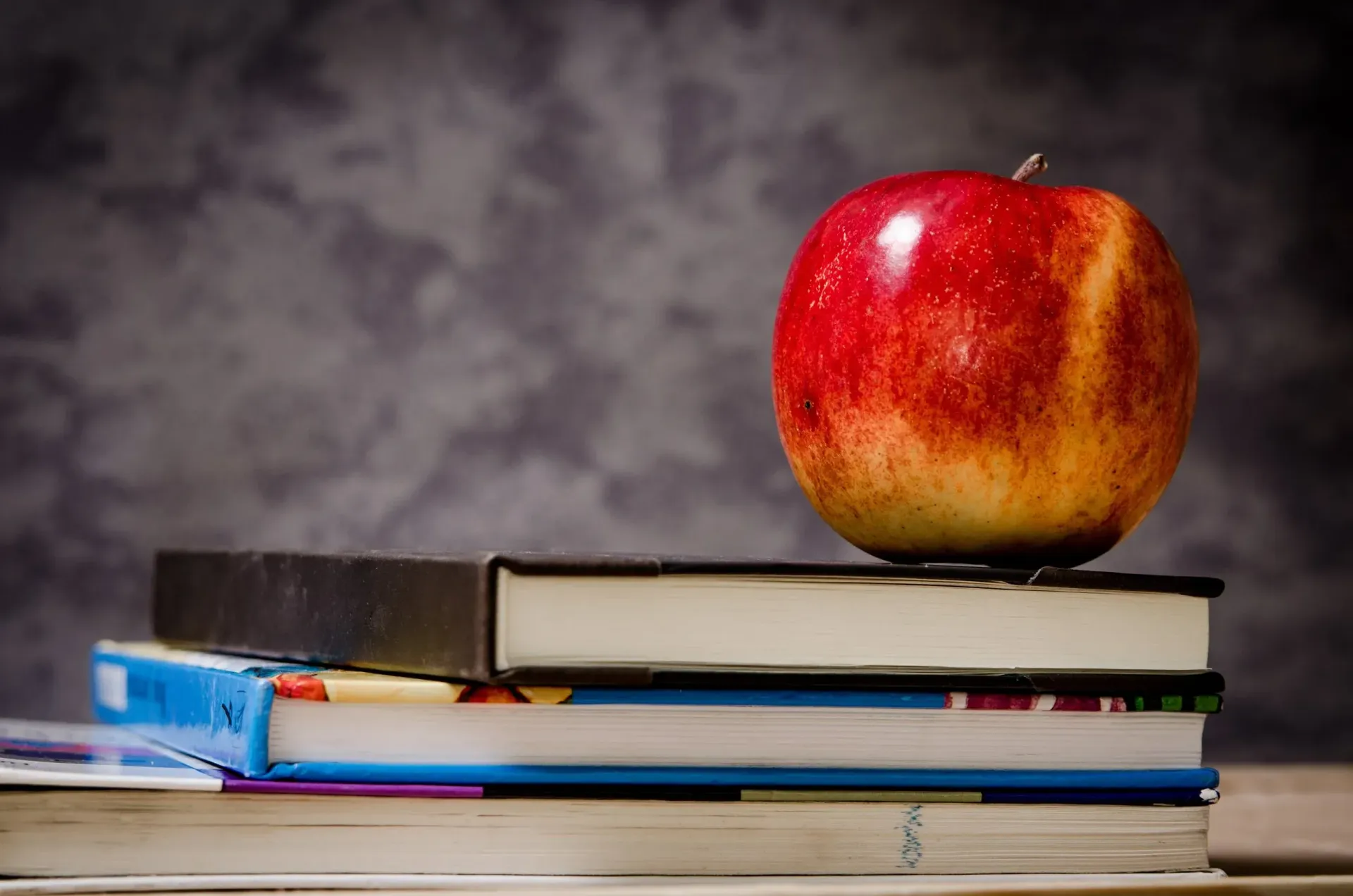 Red apple on top of a stack of books against a mottled gray background.
