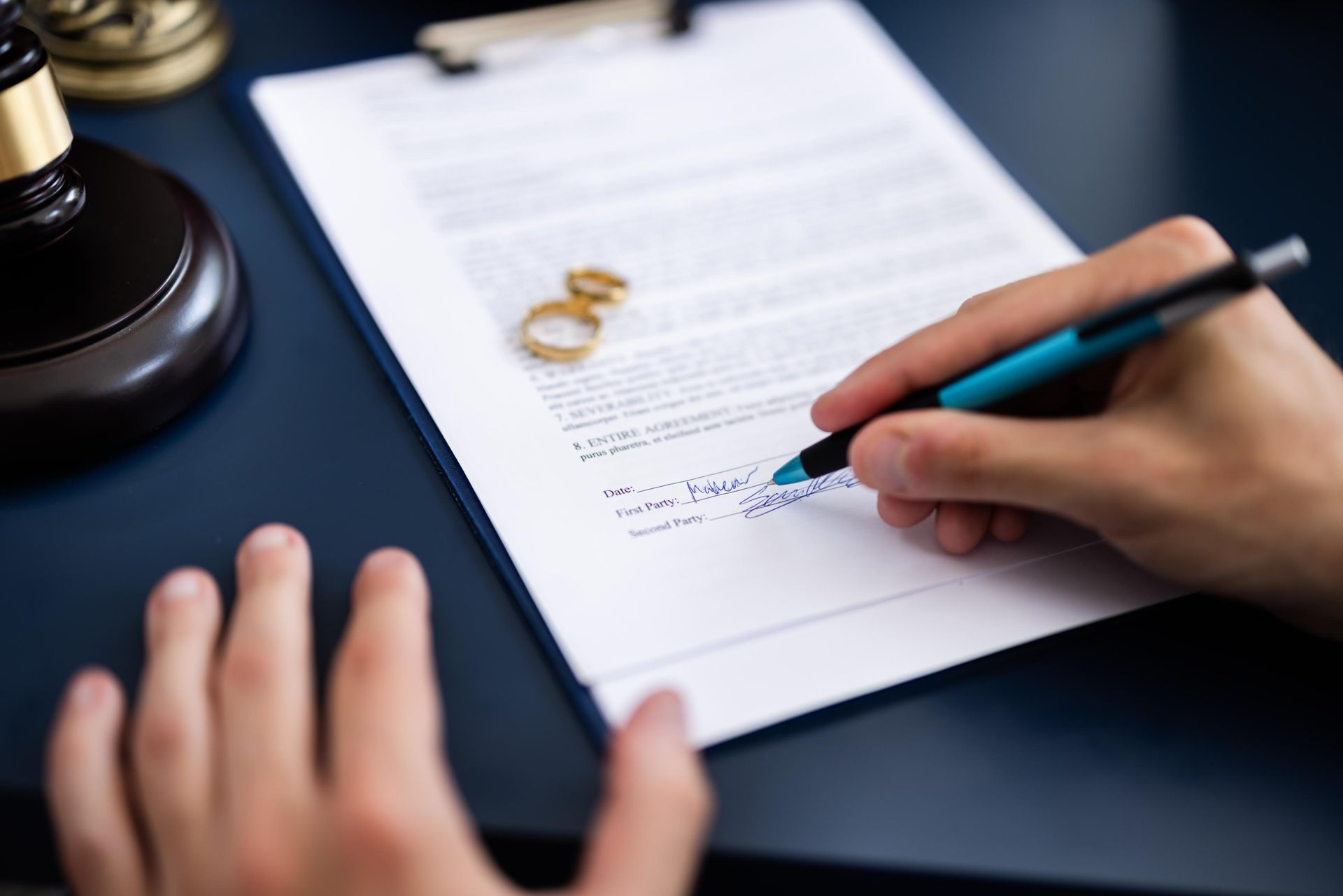Person signing divorce papers with wedding rings on the document.