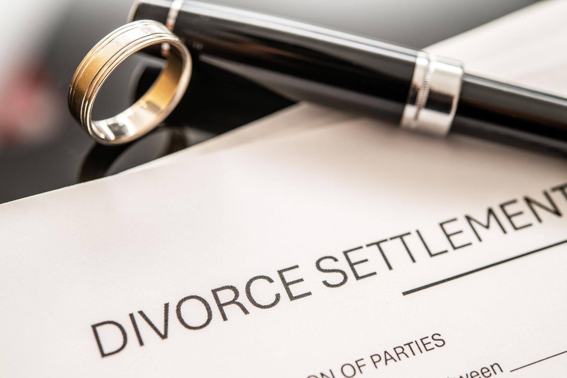 Wedding ring and pen resting on a divorce settlement document.