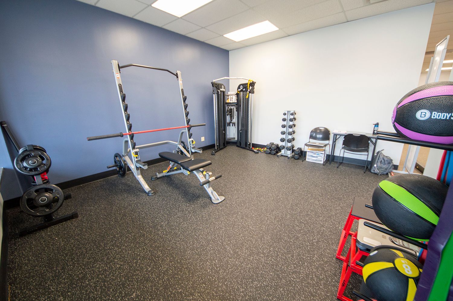 A small gym with weights, a bench, and exercise equipment against blue and white walls, on a gray floor.