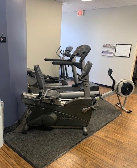 Fitness equipment in a gym setting. Includes a recumbent bike, treadmill, and rowing machine.