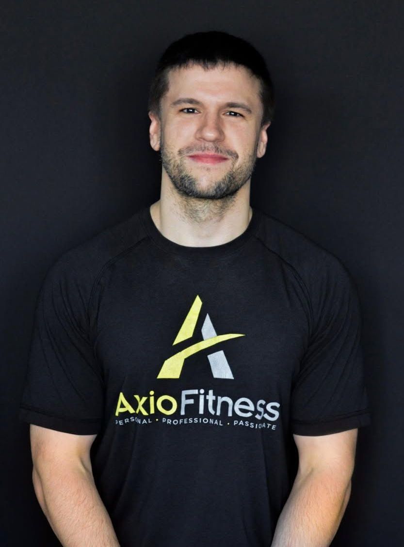 Man with short brown hair and beard wearing a black AxioFitness t-shirt against a black background.