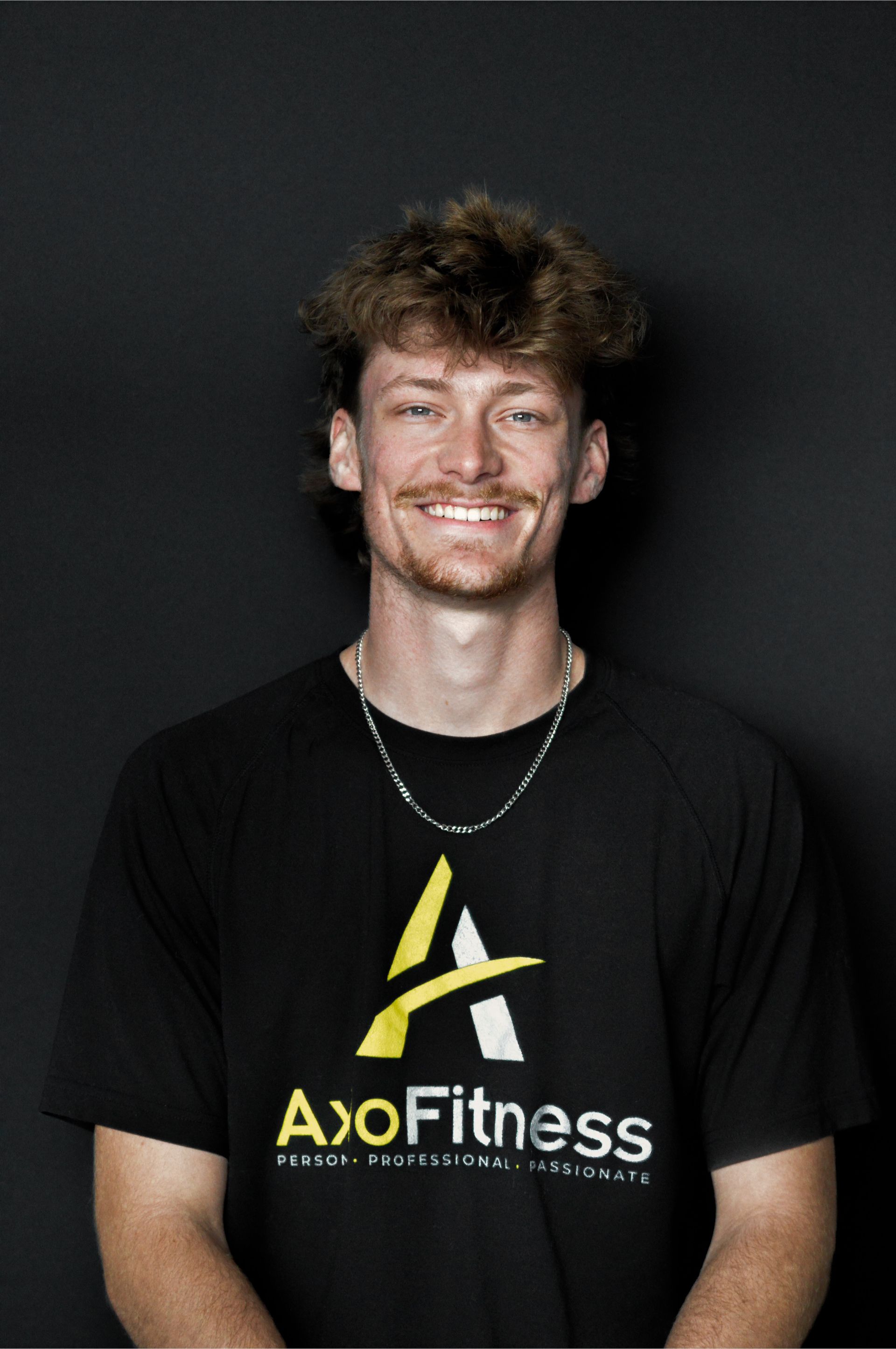 Man smiling, wearing a black AxoFitness shirt, against a dark background.