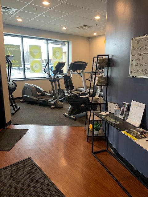 A fitness studio interior with elliptical machines by a window, and a rack of pamphlets beside a dark blue wall.