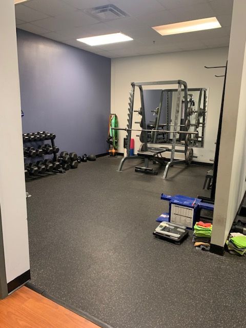 A small gym with black rubber flooring. There are dumbbells, a weight rack, and exercise equipment.
