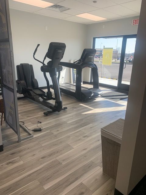 Gym with an elliptical machine and treadmill by a window. Light wood floor and neutral walls.