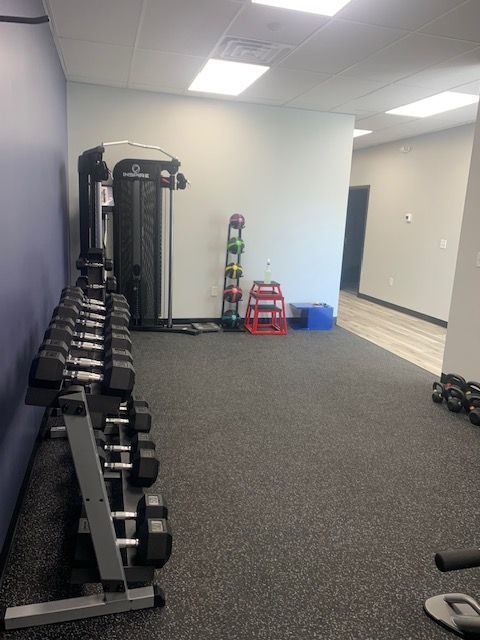 A gym interior with dumbbell racks, exercise equipment, and a doorway to another room.