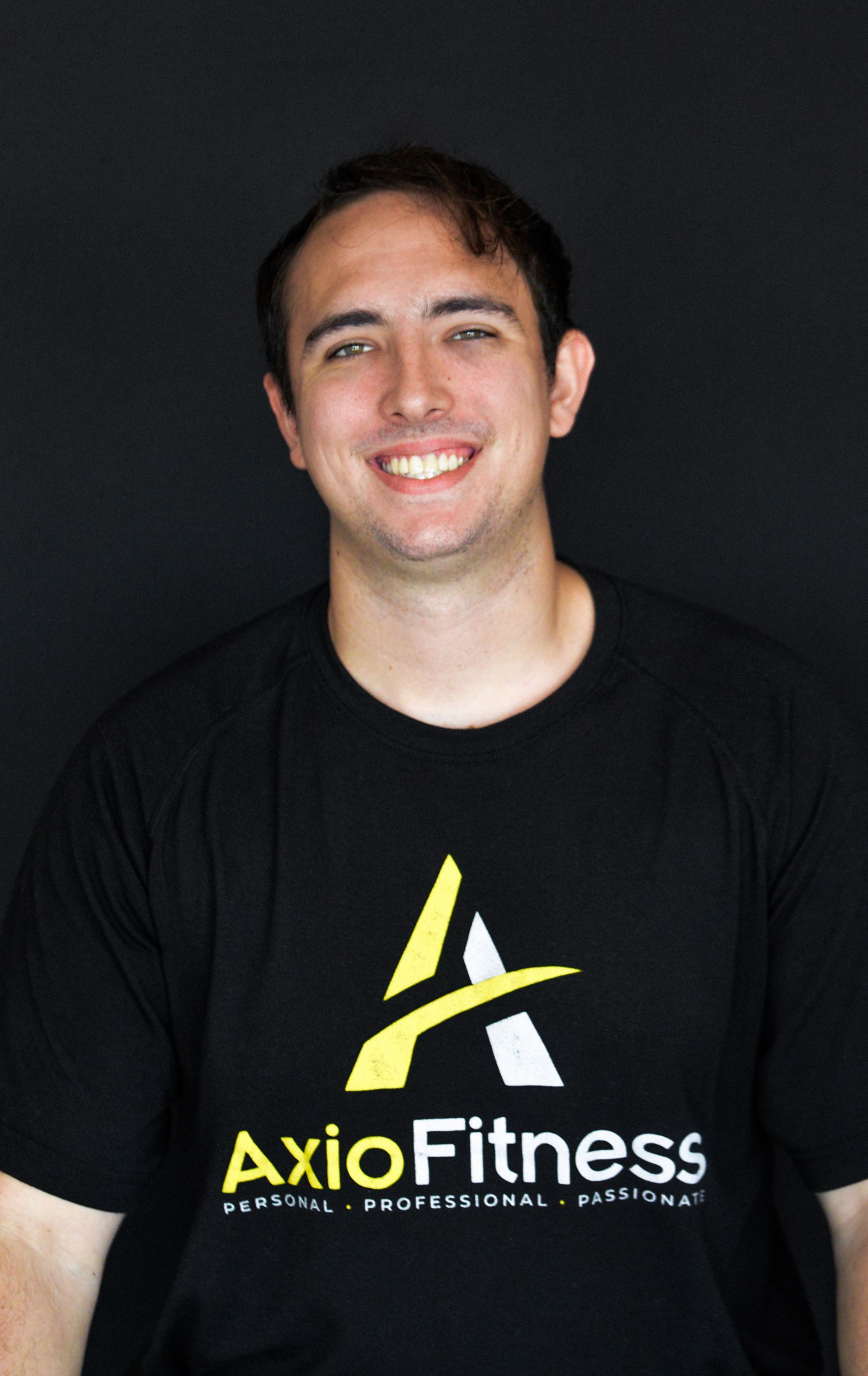 Man with brown hair smiling, wearing a black AxioFitness t-shirt. He is positioned in front of a black backdrop.
