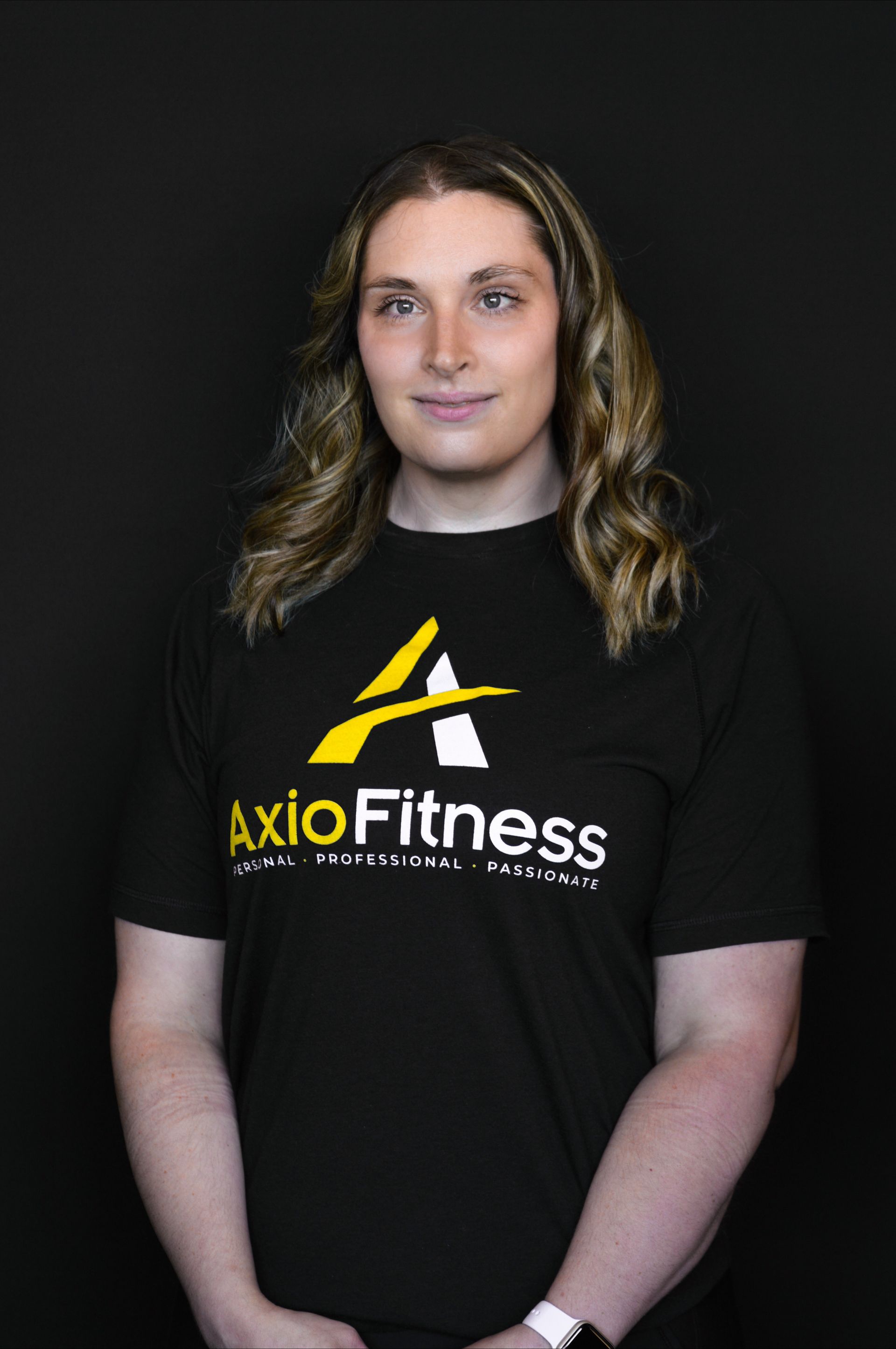 Woman in black AxioFitness T-shirt standing against a dark background, facing forward.