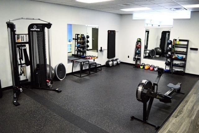 A well-equipped gym with exercise machines, weights, and mirrors on a dark rubber floor.