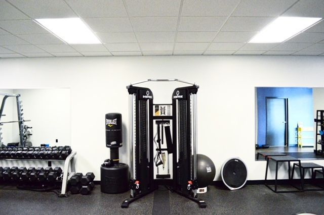 Gym interior with weight machines, free weights, a punching bag, and exercise equipment. White walls, black flooring.