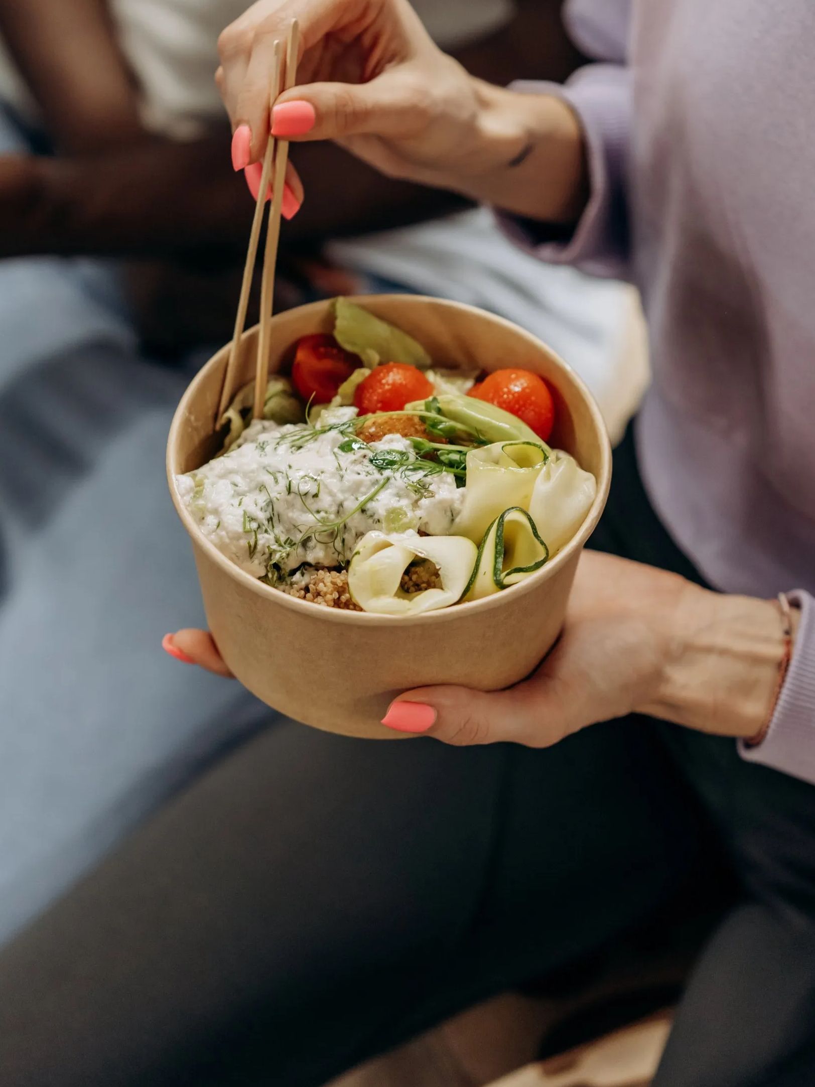 Woman holding a bowl of salad with chopsticks, eating. The salad contains rice, vegetables, and tomatoes.