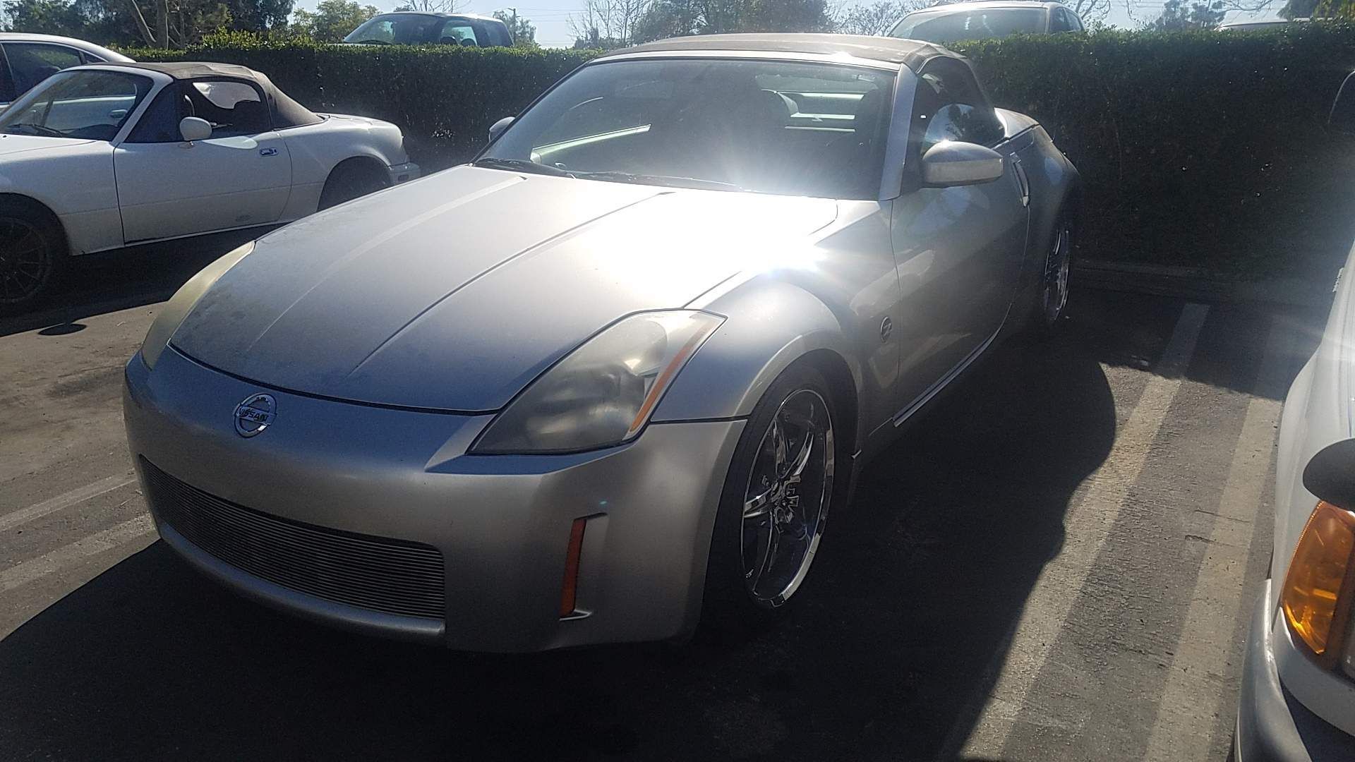 A silver sports car is parked in a parking lot next to a white car.