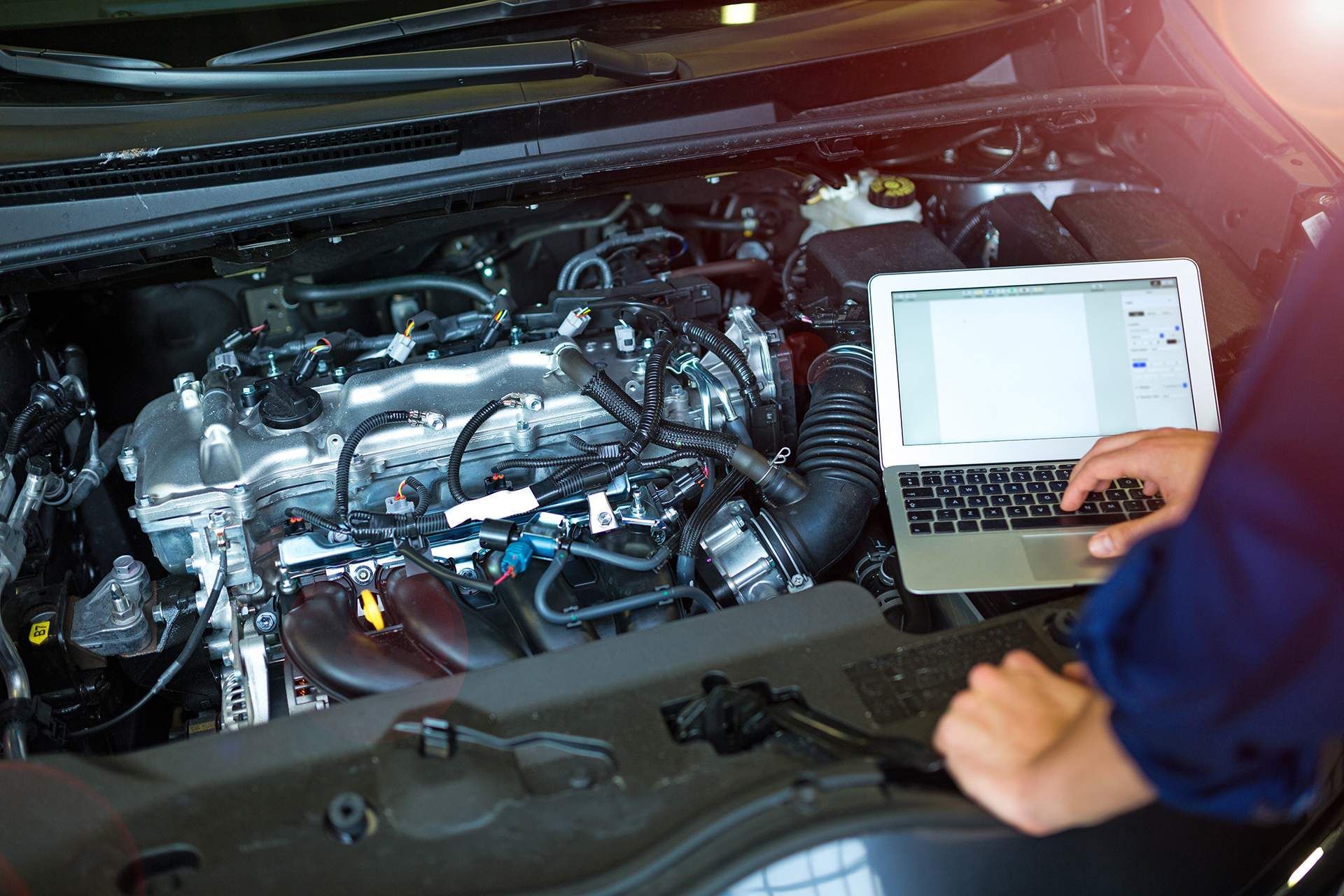 A mechanic is using a laptop computer to check the engine of a car.