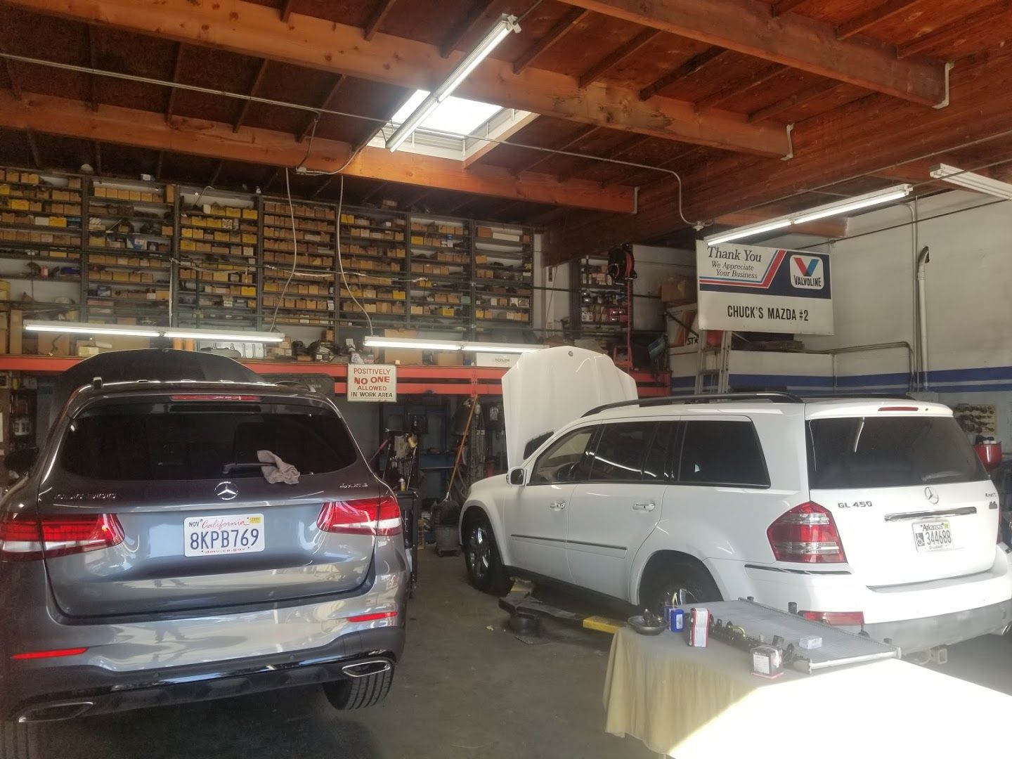 Two cars are parked in a garage with their hoods open.